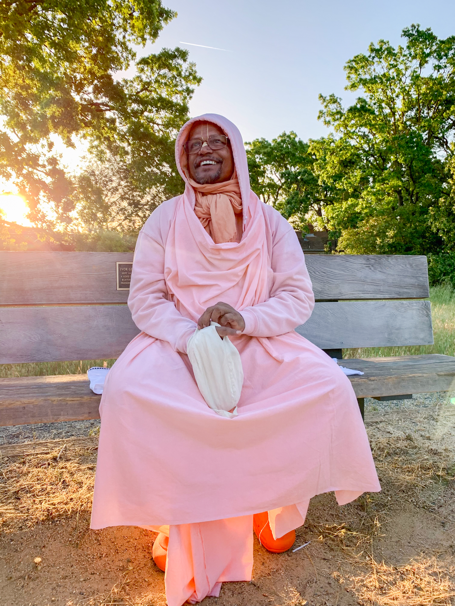 Bhakti_Swarup_Sridhar_Maharaja_Bench_Sun Srila Bhakti Swarup Sridhara Maharaja sitting on a bench backlit by the sun while chanting papa